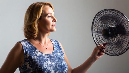 Frau mit Hitzewallungen vor einem Ventilator