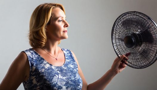 Frau mit Hitzewallungen vor einem Ventilator